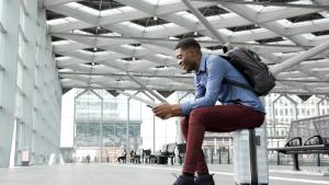 Side portrait of person sitting on suitcase at station with mobile phone