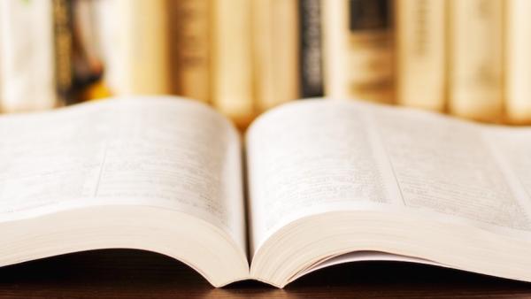 Open book on a table with a book case in the background