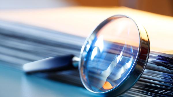 magnifying glass leaning against a stack of files of paper