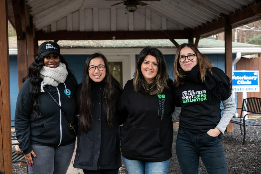 4 New Relic employees stand outside a veterinary clinic at PAWS Atlanta, smiling and wearing New Relic T-shirts and sweatshirts.